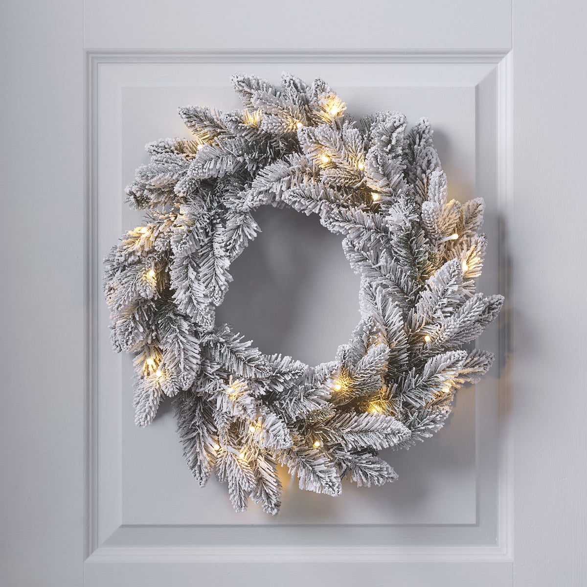 Verschneiter Weihnachtskranz mit warmweißen LEDs an weißer Tür hängend