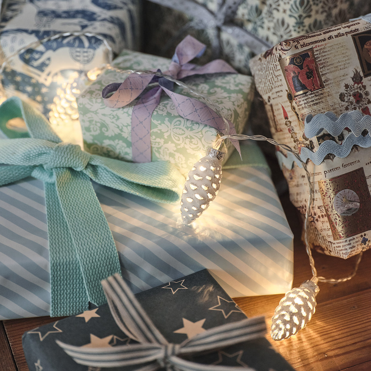 LED Lichterkette mit beleuchteten Glas-Tannenzapfen dekoriert auf Geschenkpaketen
