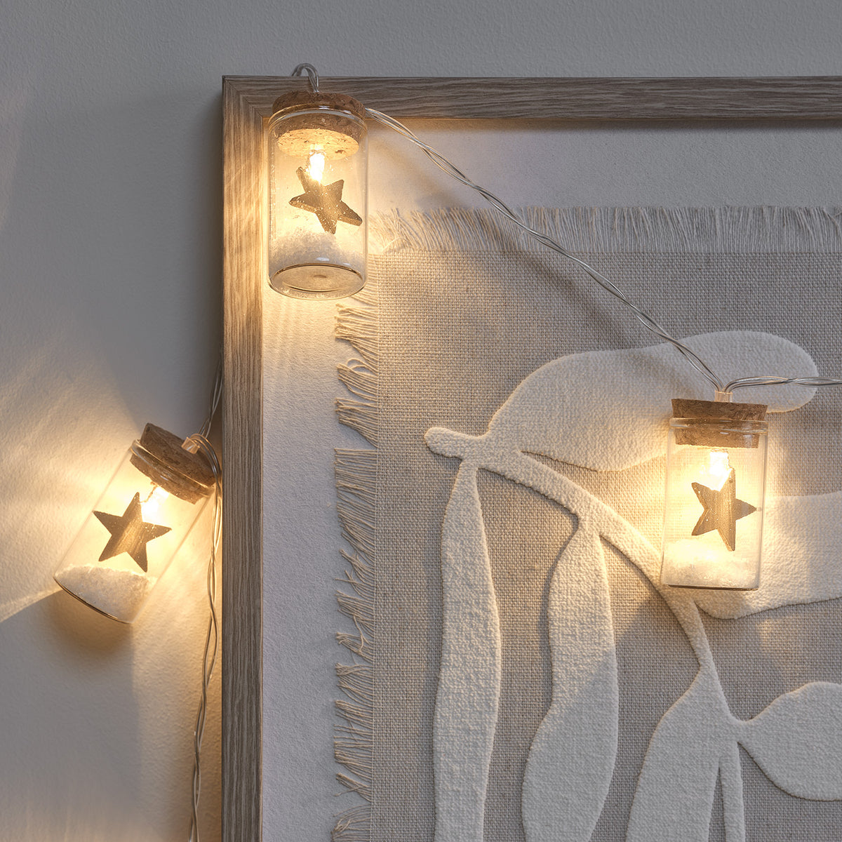 LED-Lichterkette mit kleinen Glasfläschchen, goldener Stern und Kunstschnee an Wandbild