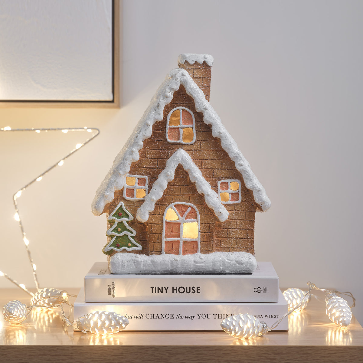 Keramik-Lebkuchenhaus mit Schnee und warmweißer LED-Beleuchtung, auf Büchern mit Lichterkette