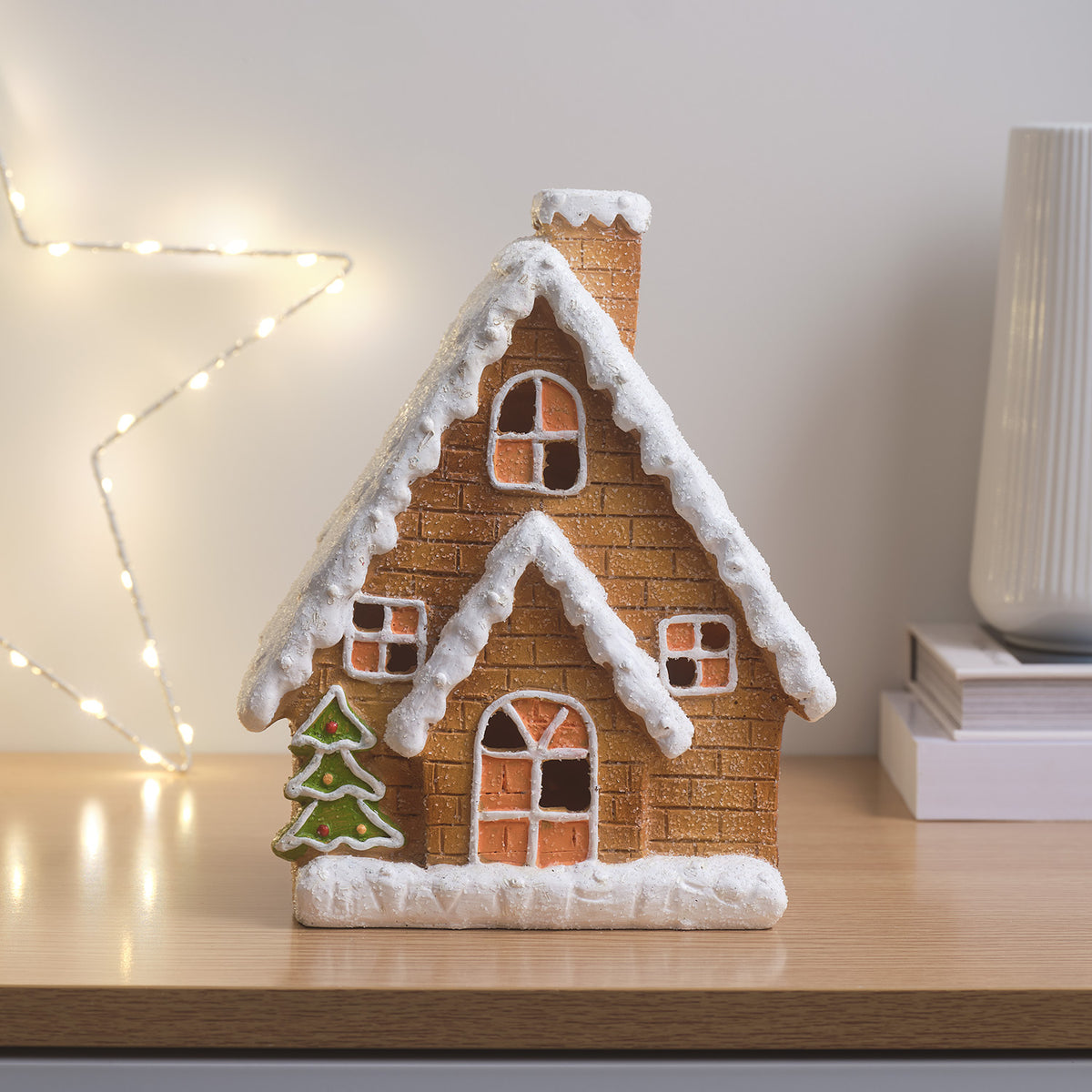 Lebkuchenhaus mit eingeschalteter LED-Beleuchtung, dekoriert mit Weihnachtsbaum und Schnee
