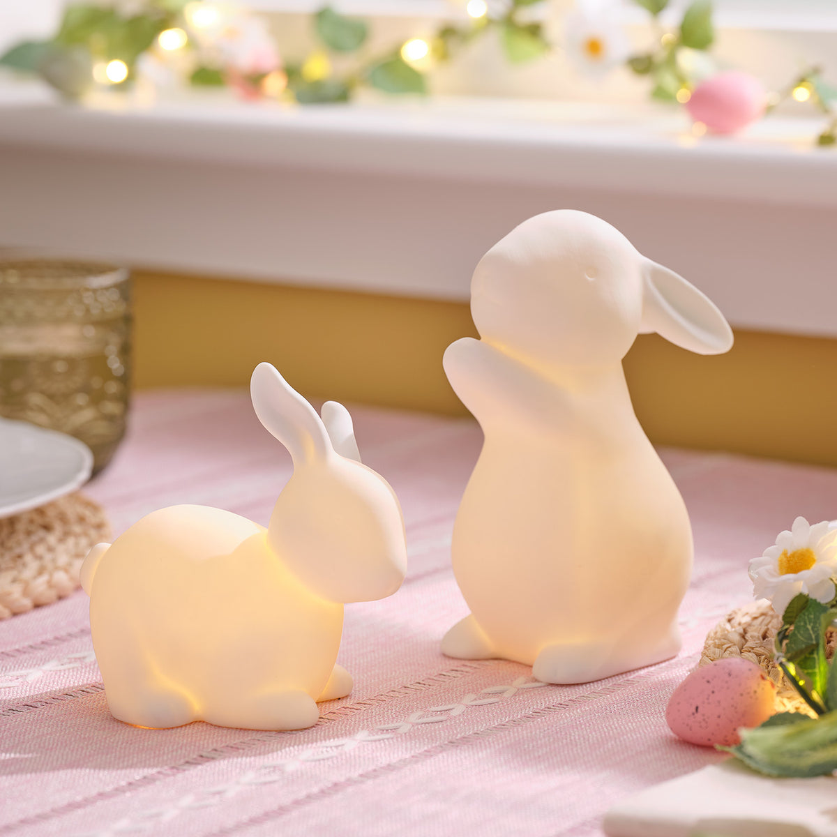 Beleuchtete Porzellan-Osterhasen auf rosa Tischdecke mit Osterdeko und Eiern