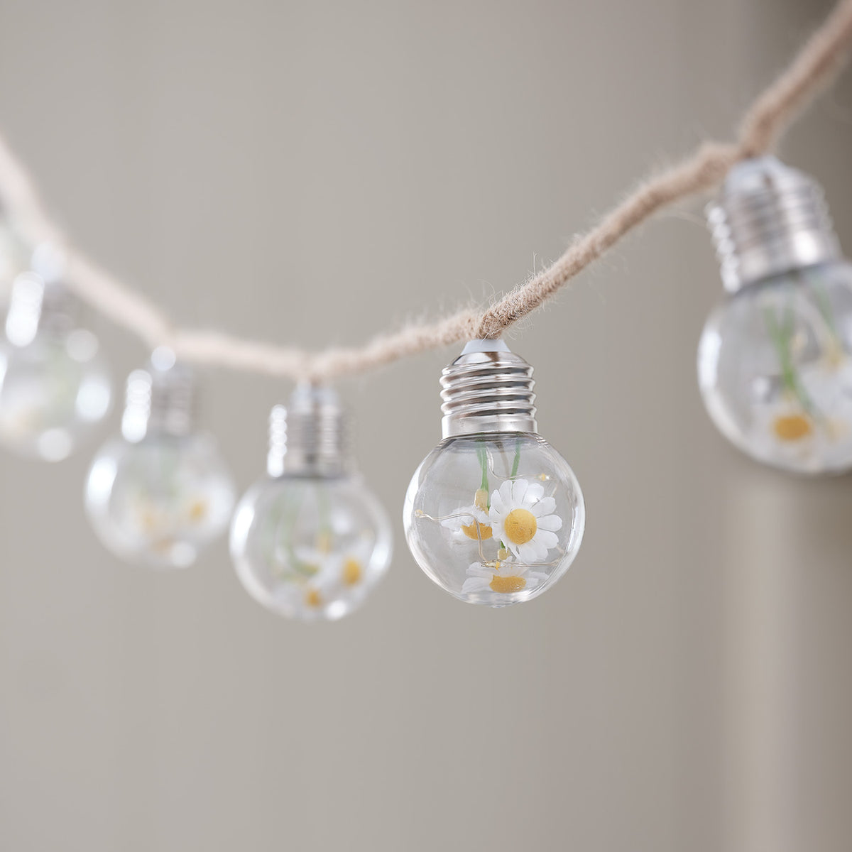 Detailaufnahme einer Glühbirne mit Gänseblümchen und warmweißen LEDs an Juteseil