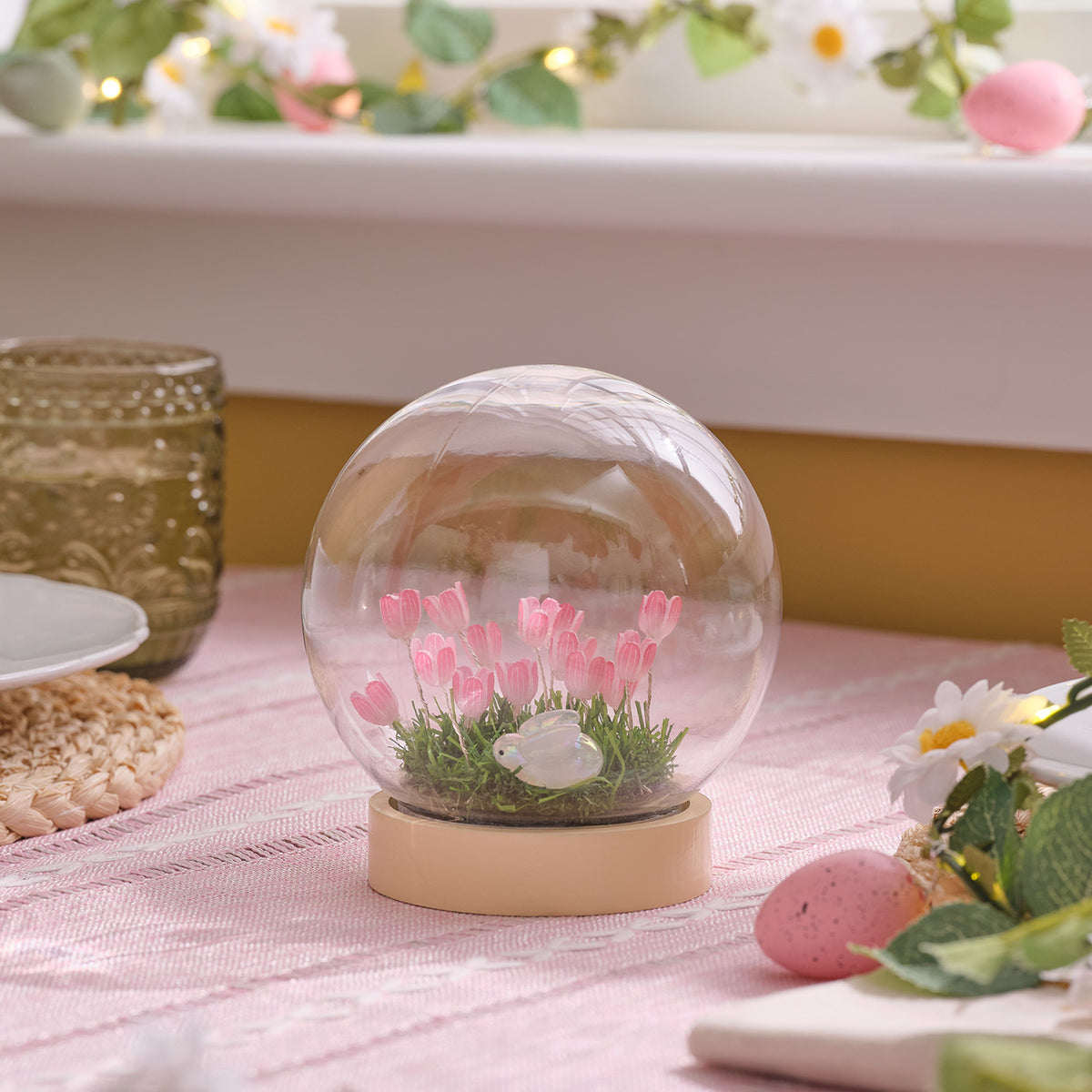 LED-Osterkugel mit rosa Tulpen und Hasenfigur in klarer Kuppel auf rosa Tischdecke
