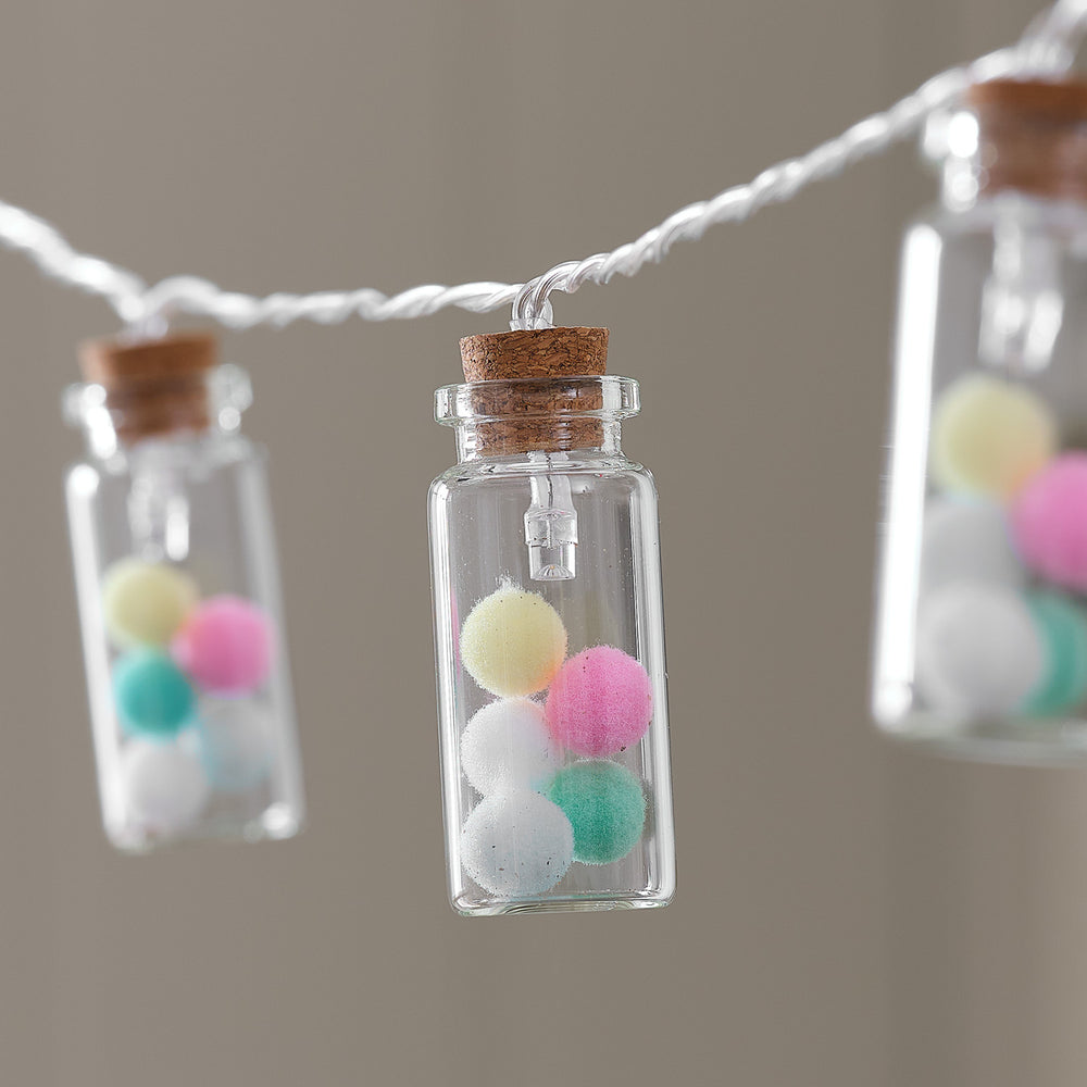 Glasfläschchen mit bunten Pompoms ohne LED-Beleuchtung an transparenter LED-Lichterkette