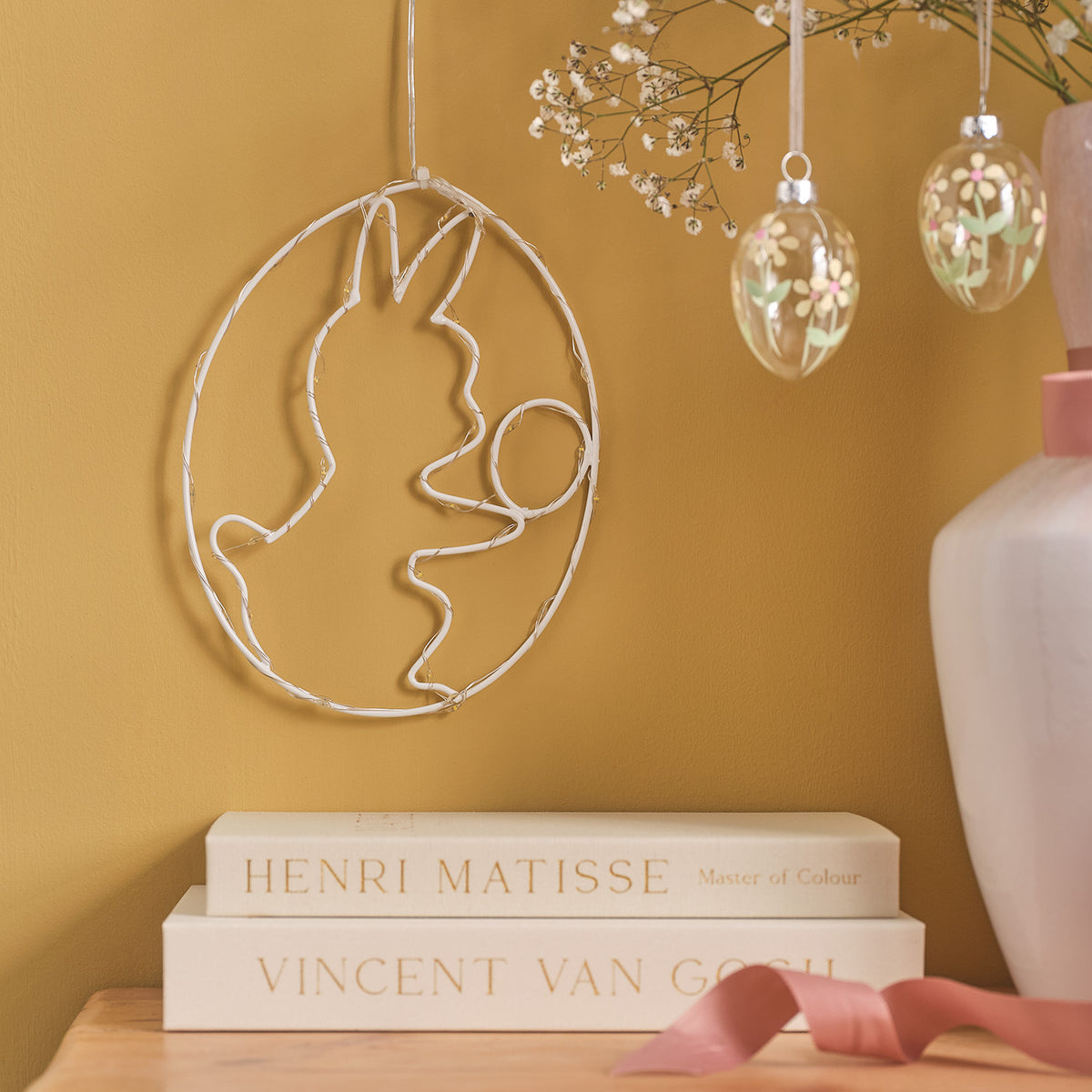 LED-Osterei mit Häschen-Motiv aus weißem Metallrahmen ohne Beleuchtung an gelber Wand