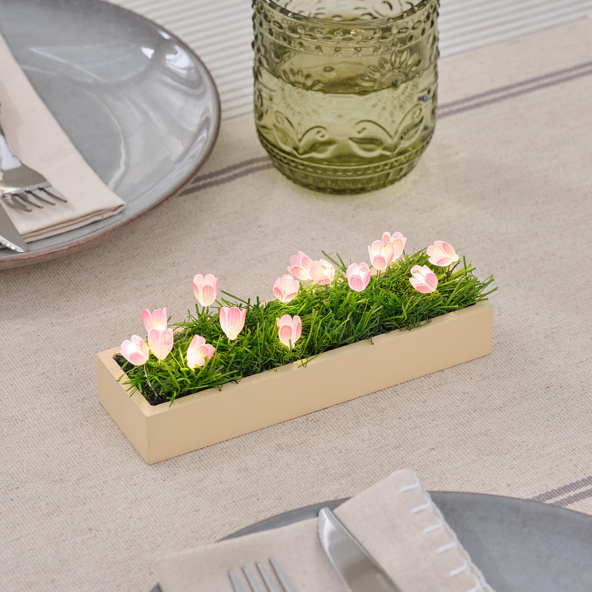 Mini LED-Tulpen Tischdeko mit rosa Tulpen und warmweißen LEDs auf Holzsockel auf gedecktem Tisch