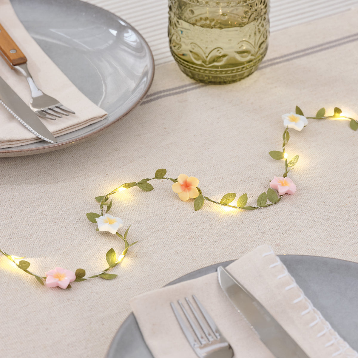 Mikro LED-Lichterkette mit pastellfarbenen Blumen und grünen Blättern auf gedecktem Tisch