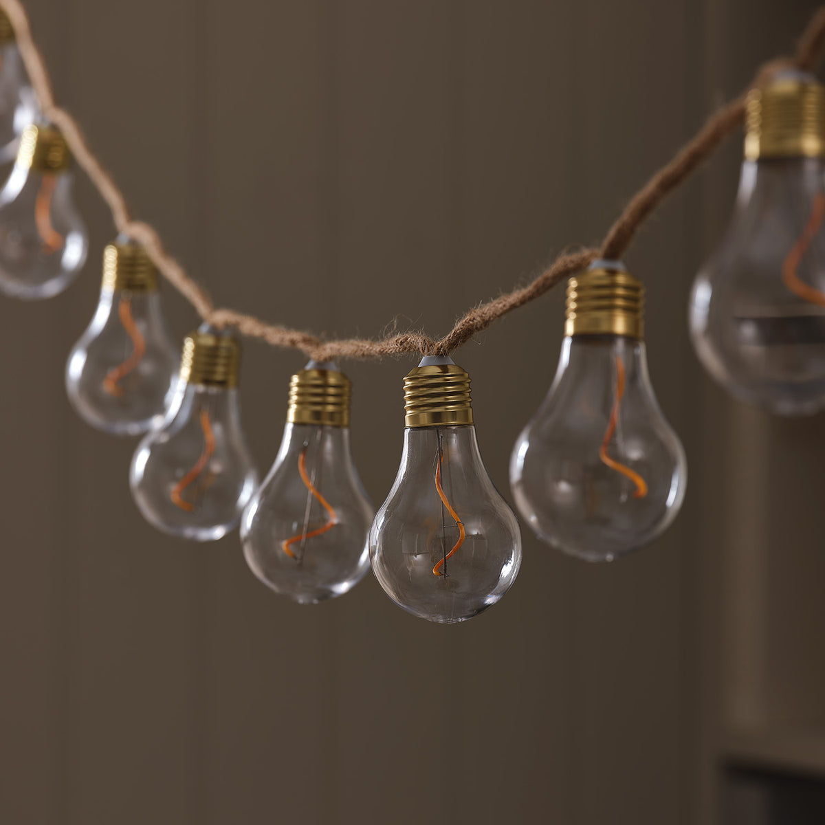 LED-Glühbirnen-Lichterkette mit transparenten Birnen und goldfarbenen Fassungen an Naturseil