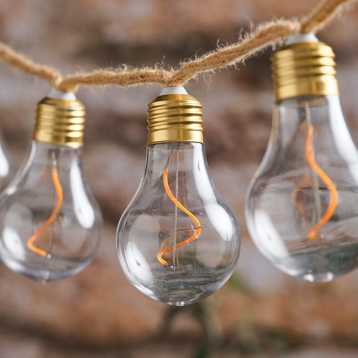 Nahaufnahme LED-Glühbirnen mit sichtbarem Filament an rustikalem Naturseil vor braunem Hintergrund
