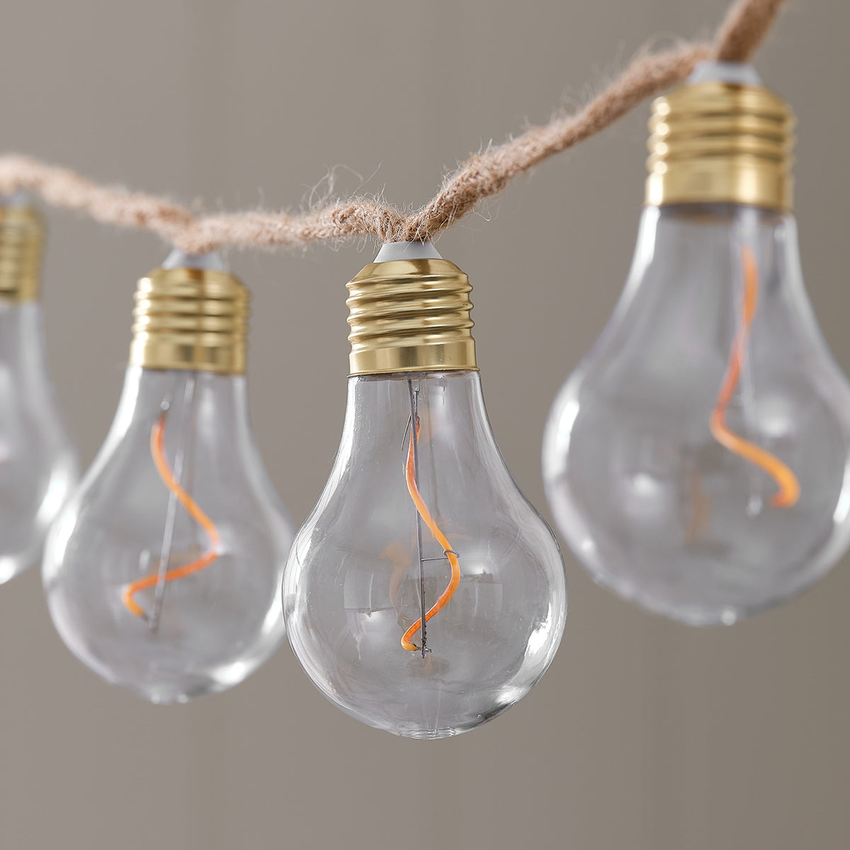 Detailaufnahme transparente LED-Glühbirnen mit goldfarbenem Sockel an Naturseil