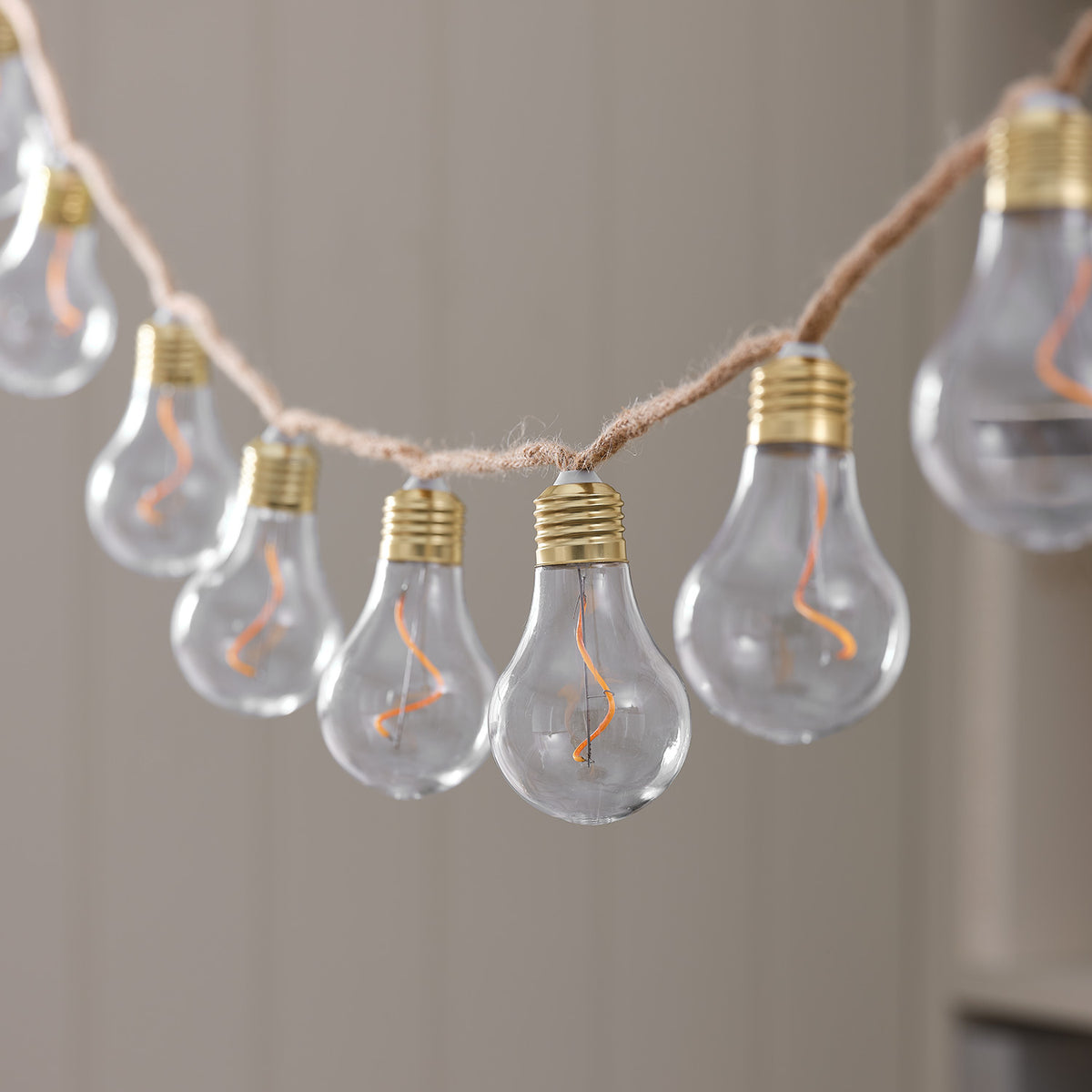 Nahaufnahme transparente LED-Glühbirne mit sichtbarem Filament und goldfarbenem Sockel an Naturseil