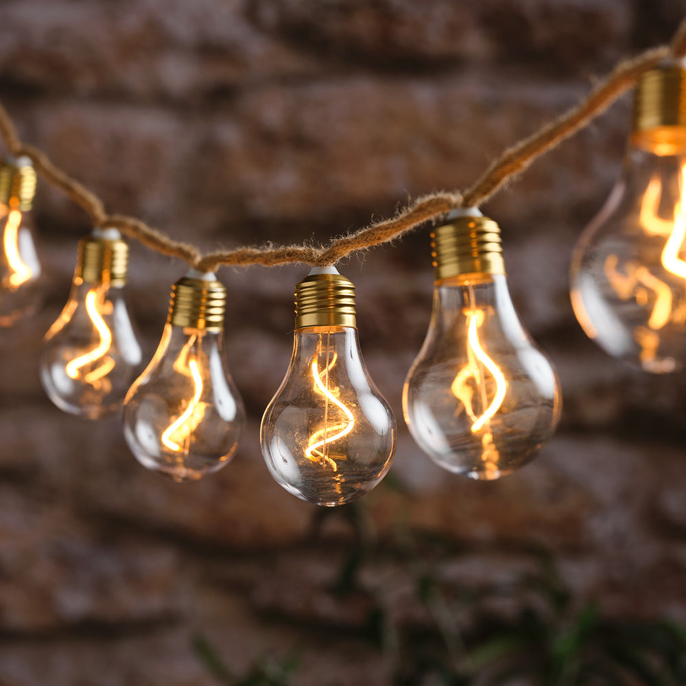 LED-Glühbirnen-Lichterkette mit warmweiß leuchtenden Filament-Birnen an Naturseil vor Backsteinwand