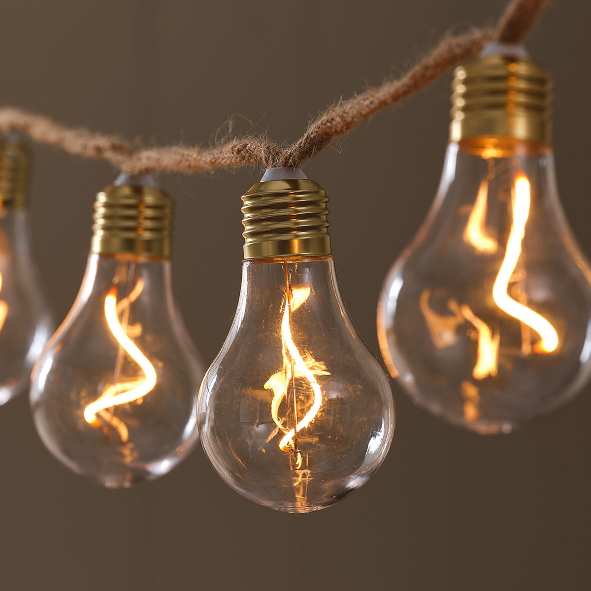 Nahaufnahme transparente LED-Glühbirne mit goldfarbenem Sockel an rustikalem Naturseil
