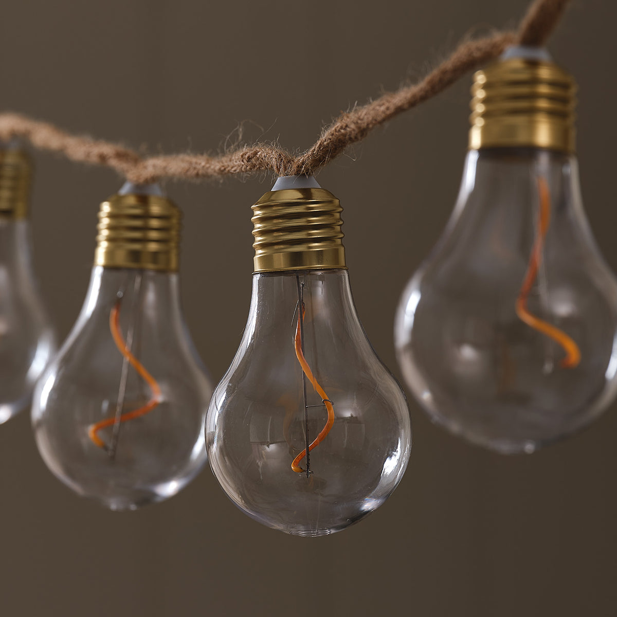 LED-Glühbirnen-Lichterkette mit warmweiß leuchtenden Filament-Birnen an Naturseil vor braunem Hintergrund