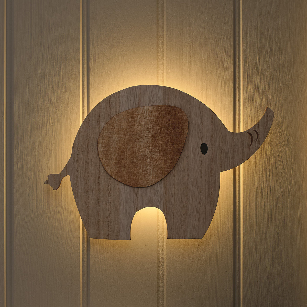 Holzlampe in Elefantenform leuchtet warmweiß an einer hellen Wand