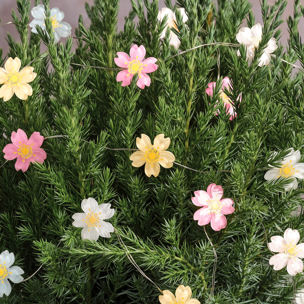 Pastellfarbene Blumenlichterkette dekorativ in grünen Zweigen drapiert