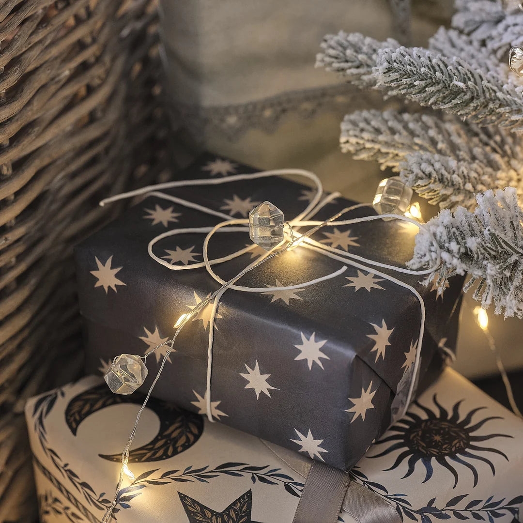 Lichterkette mit Kristallanhängern um Geschenk mit Sternenmuster-Papier.