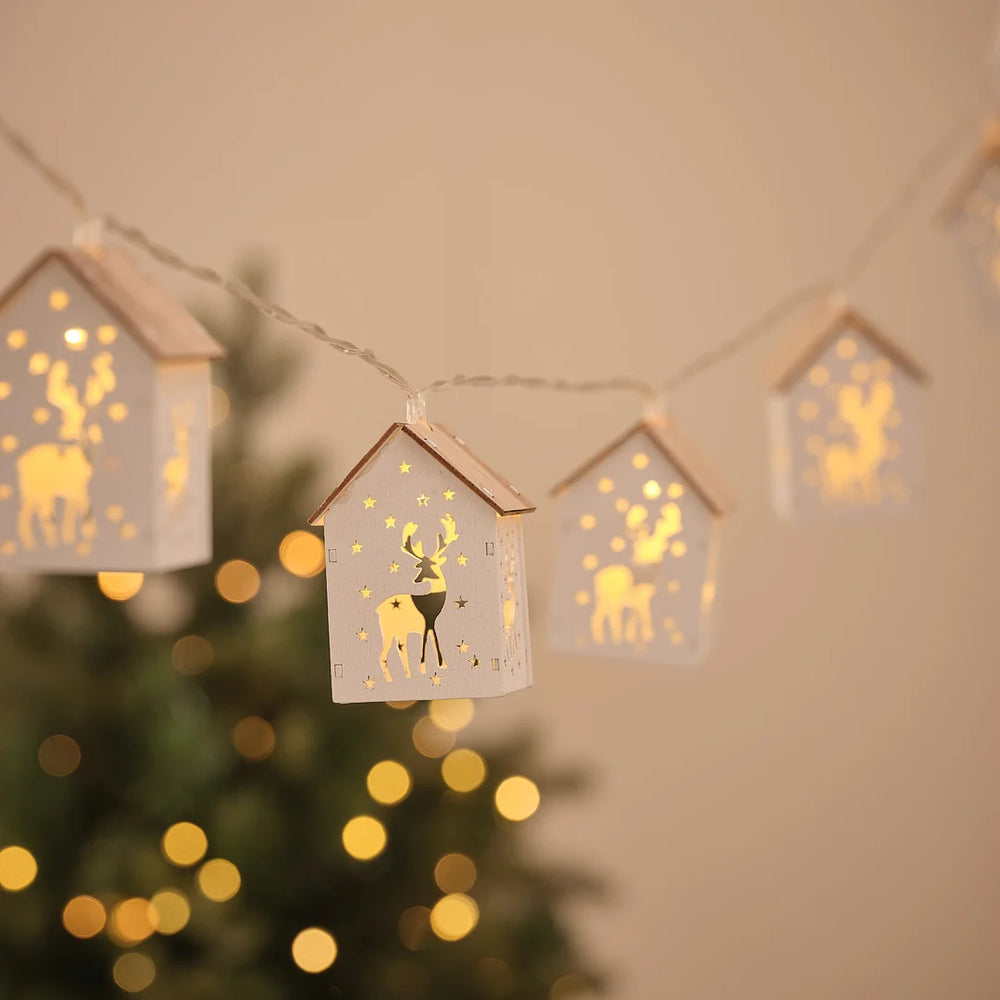 Lichterkette mit Häuschen-Anhängern mit Rentiermotiv vor Weihnachtsbaum und Lichterglanz.