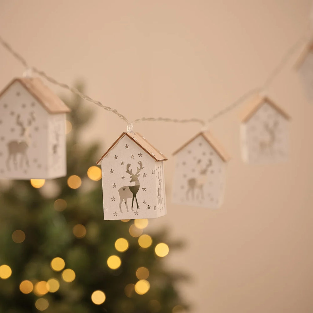 Lichterkette mit mehreren Häuschen-Anhängern mit Rentiermotiv vor Tannengrün.