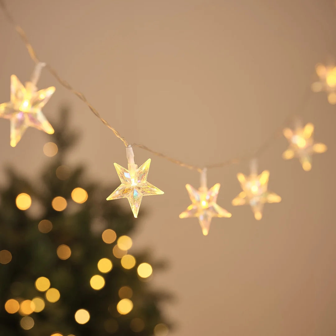 LED-Lichterkette mit irisierenden Stern-Anhängern vor Weihnachtsbaum und Lichterglanz.