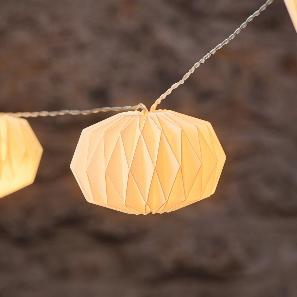 Weißer Papierlampion mit geometrischem Muster an LED-Lichterkette vor unscharfem Hintergrund