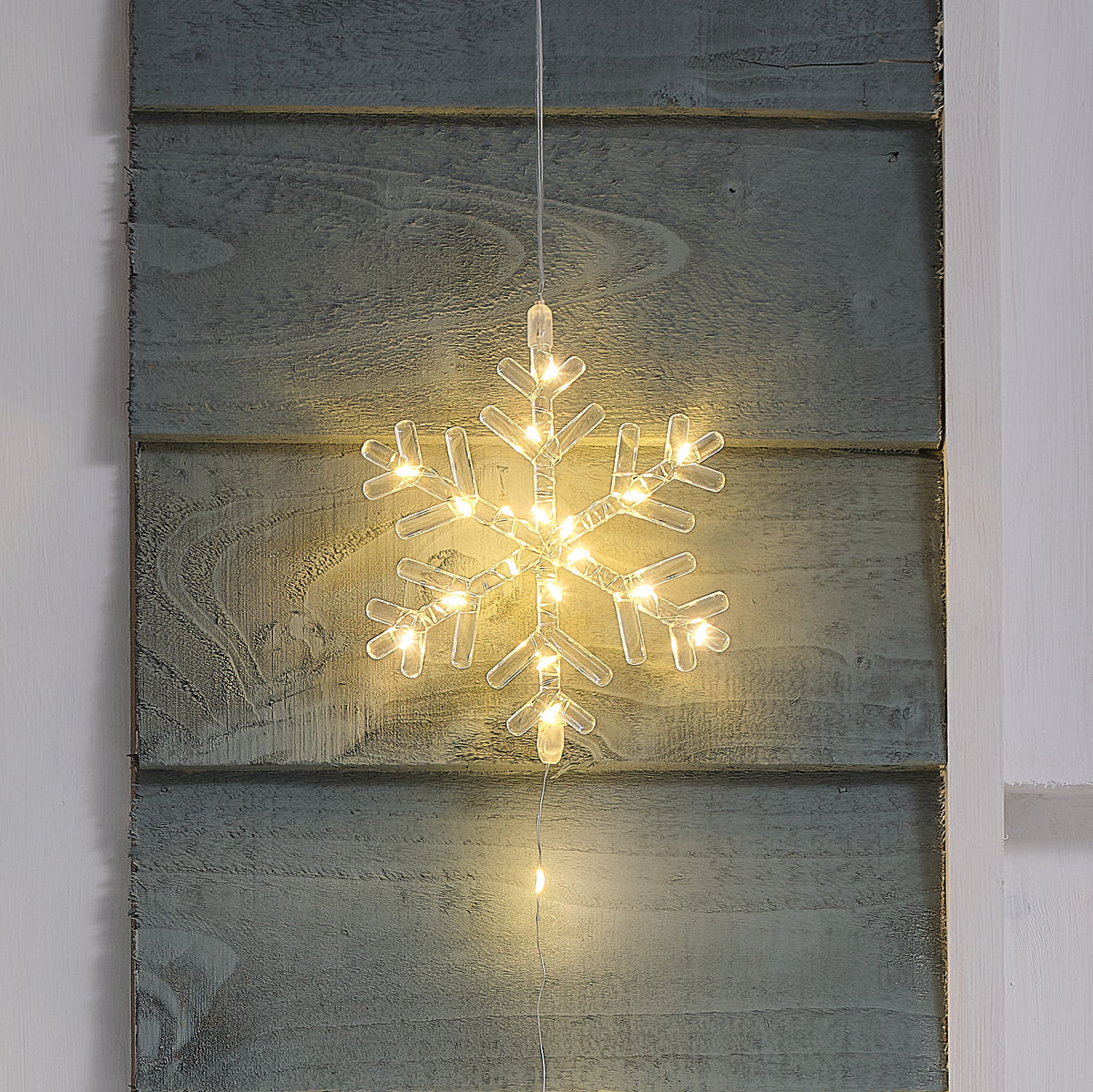 Nahaufnahme einer warmweiß leuchtenden LED-Schneeflocke aus transparentem Acryl an einer Holzfassade