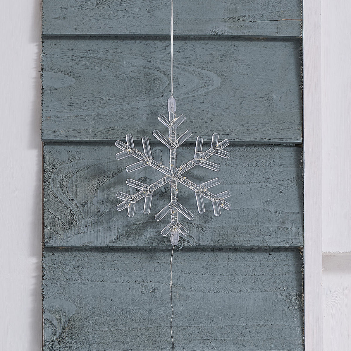 Nahaufnahme einer unbeleuchteten transparenten Acryl-Schneeflocke an einer Holzfassade