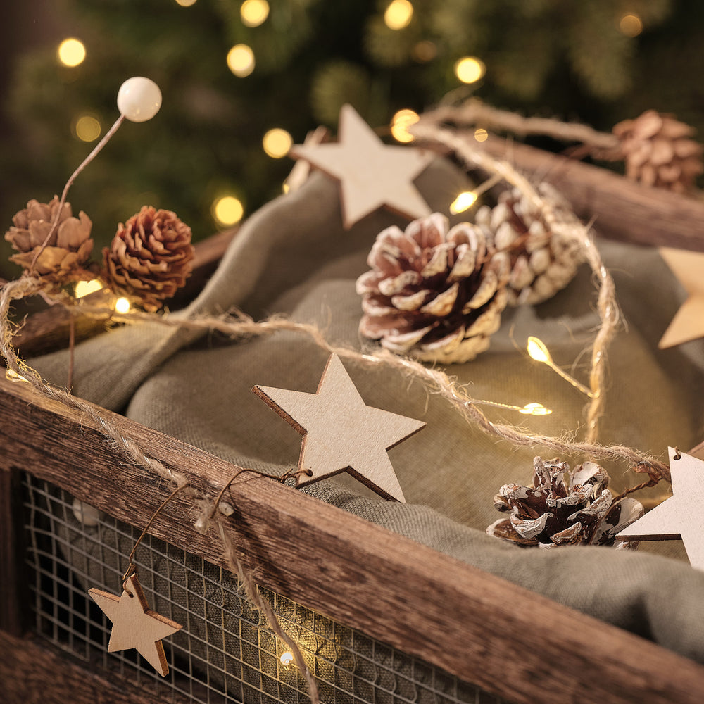 LED-Girlande mit warmweißen Lichtern, Holzsternen und Tannenzapfen auf grünem Stoff in Holzkiste