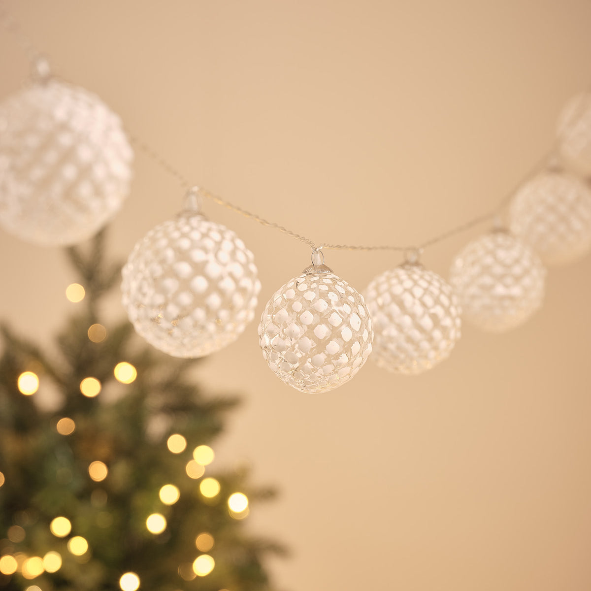 Gefrostete Glaskugeln der LED-Lichterkette in warmweißem Licht vor unscharfem Weihnachtsbaum