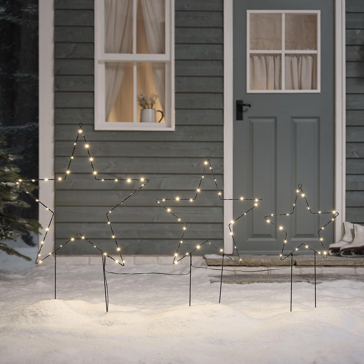 Drei unterschiedlich große LED-Sterne als Gartenstecker mit warmweißem Licht vor Haustür im Schnee