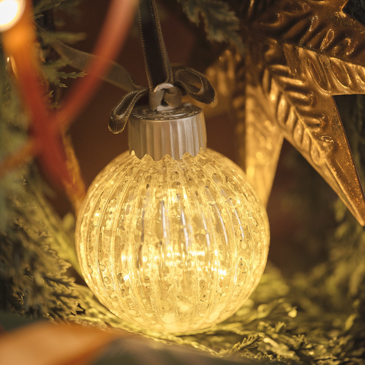 Leuchtende LED-Weihnachtskugel aus geriffeltem Glas am Weihnachtsbaum mit warmweißem Licht