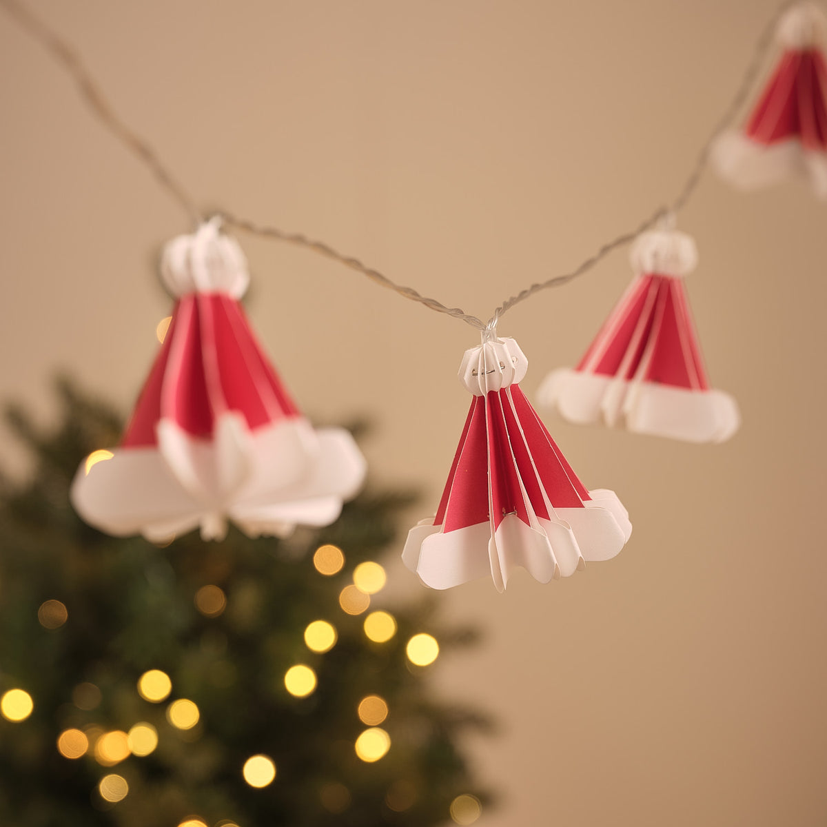 Zwei rote Papier-Weihnachtsmützen mit warmweiß leuchtenden LEDs an transparenter Lichterkette