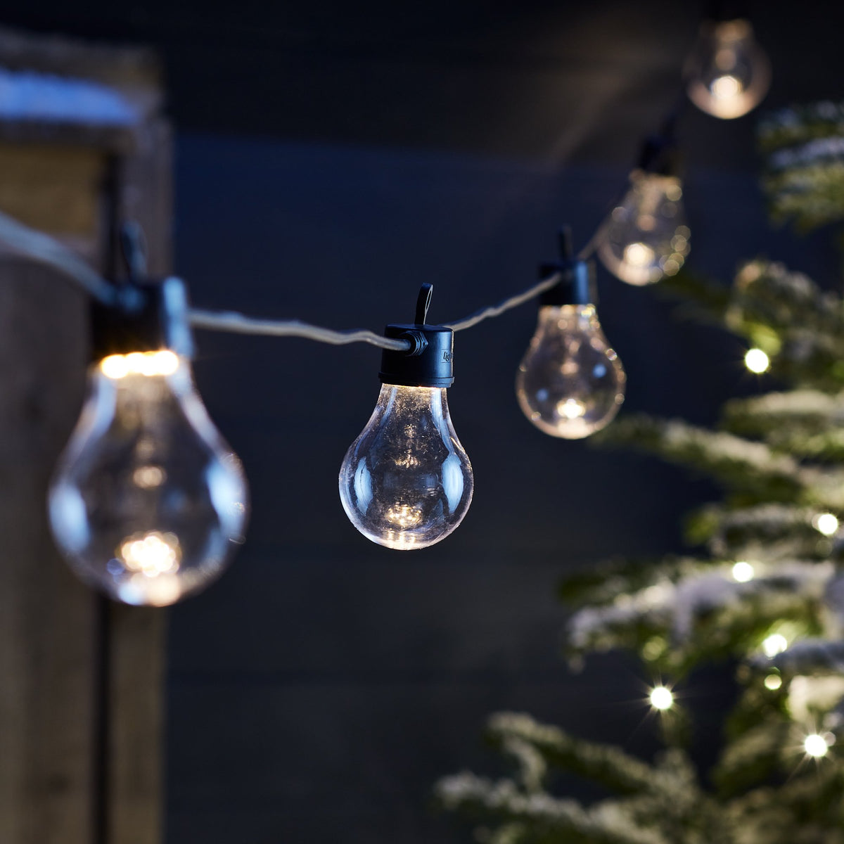 Detailaufnahme einer warmweißen Glühbirne an schwarzer Lichterkette vor dunklem Hintergrund