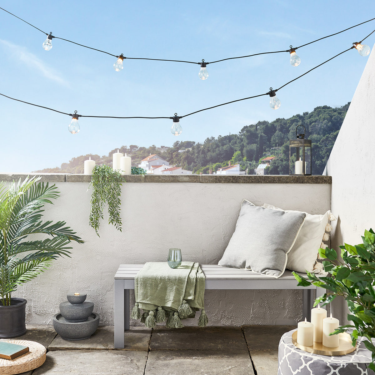 Schwarze Lichterkette mit warmweißen Glühbirnen auf Balkon mit Sitzbank und Kerzen
