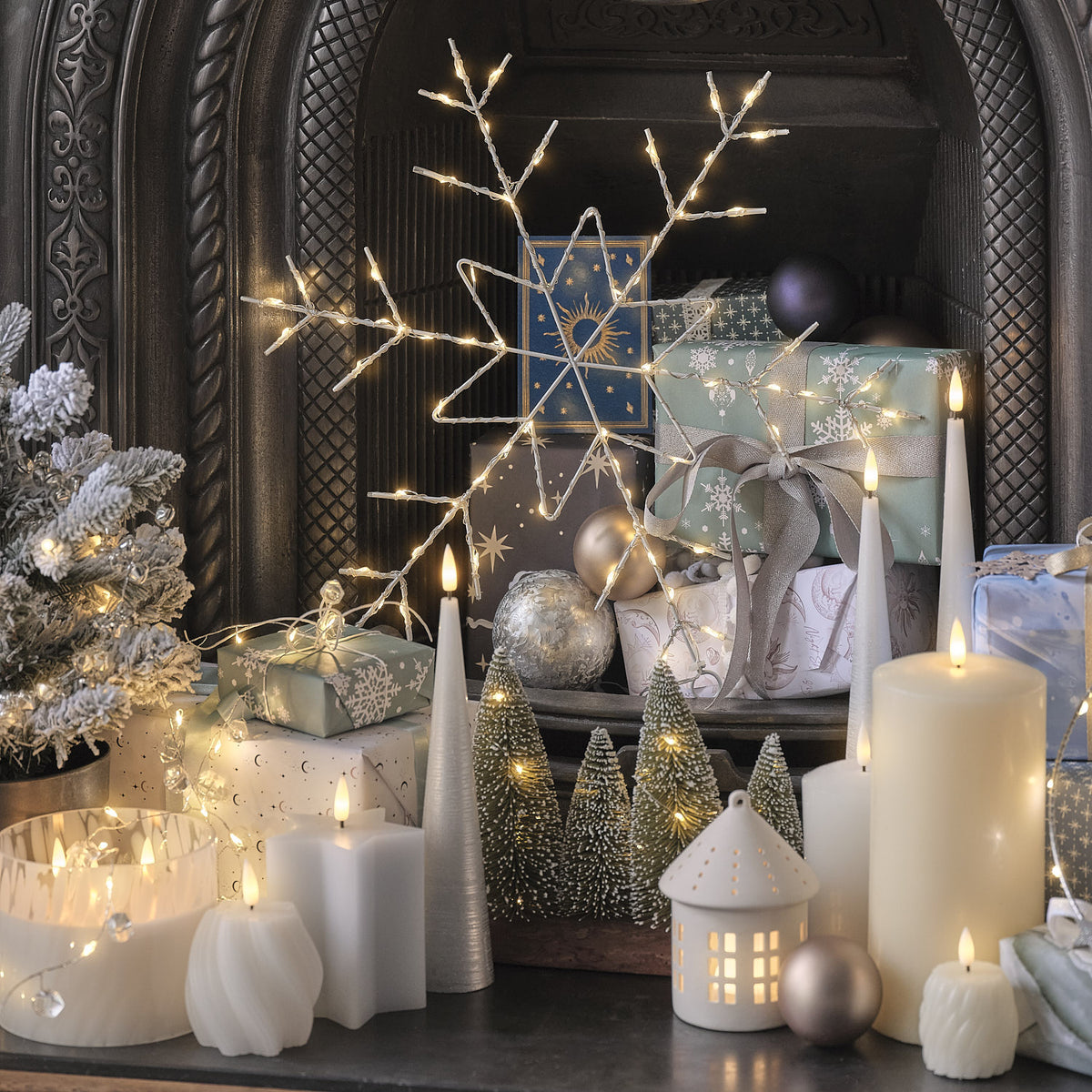 Weihnachtliche Dekoration mit Mini-Tannenbäumen, Kerzen, Geschenken und beleuchteter Schneeflocke