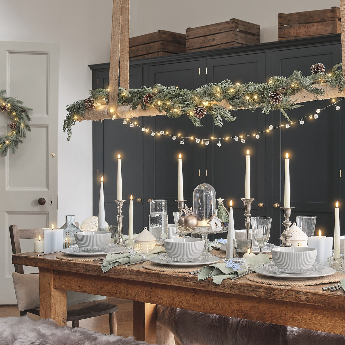 Weihnachtlich gedeckter Holztisch mit LED-Glasglocke, Kerzen, Geschirr und Tannenzweig-Hängelampe