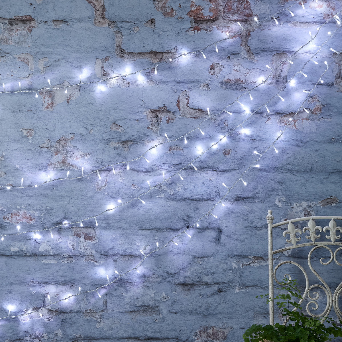 Bicolor LED Lichterkette kaltweiß an alter Backsteinwand drapiert mit Metallstuhl