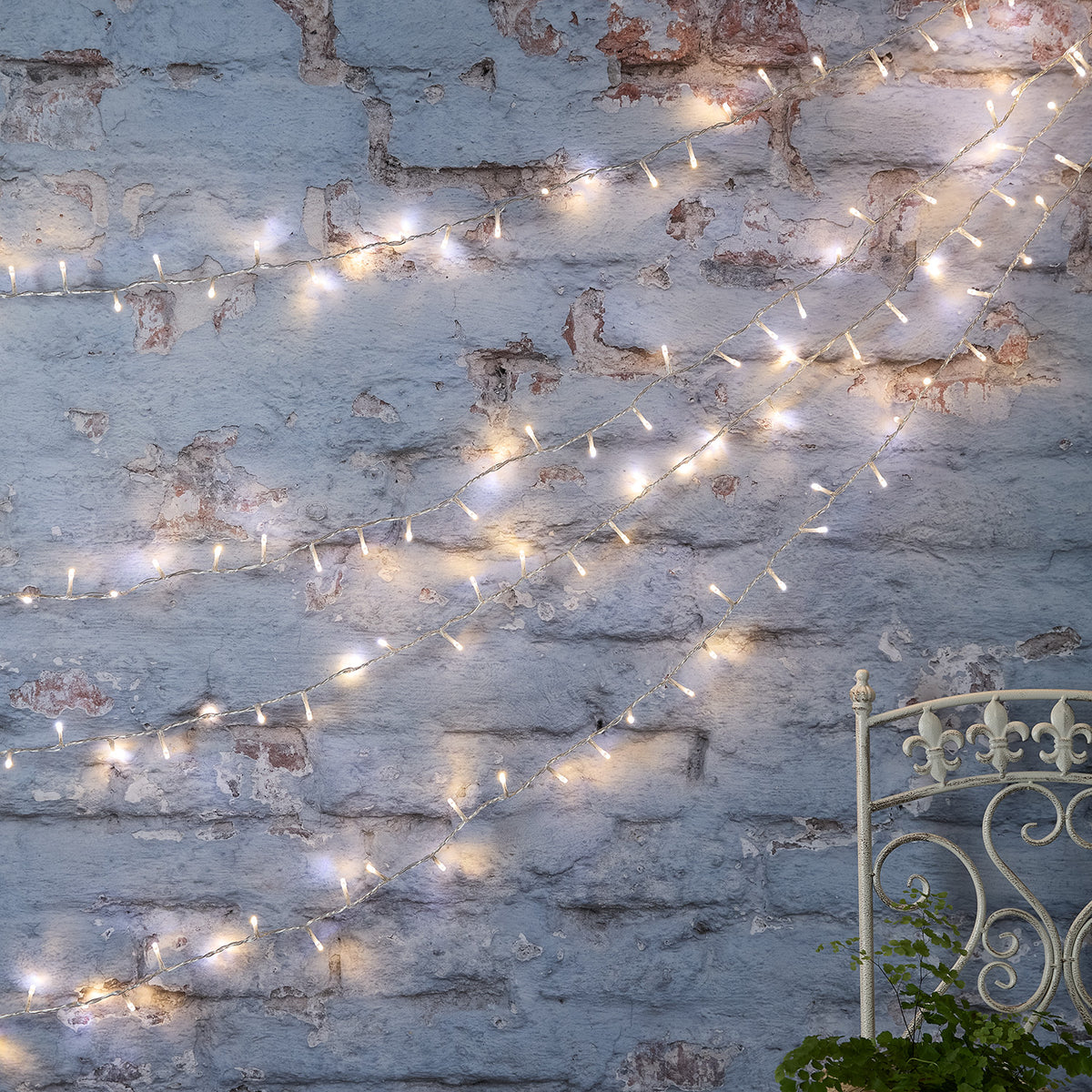 Bicolor LED Lichterkette kaltweiß an alter Backsteinwand drapiert mit Metallstuhl