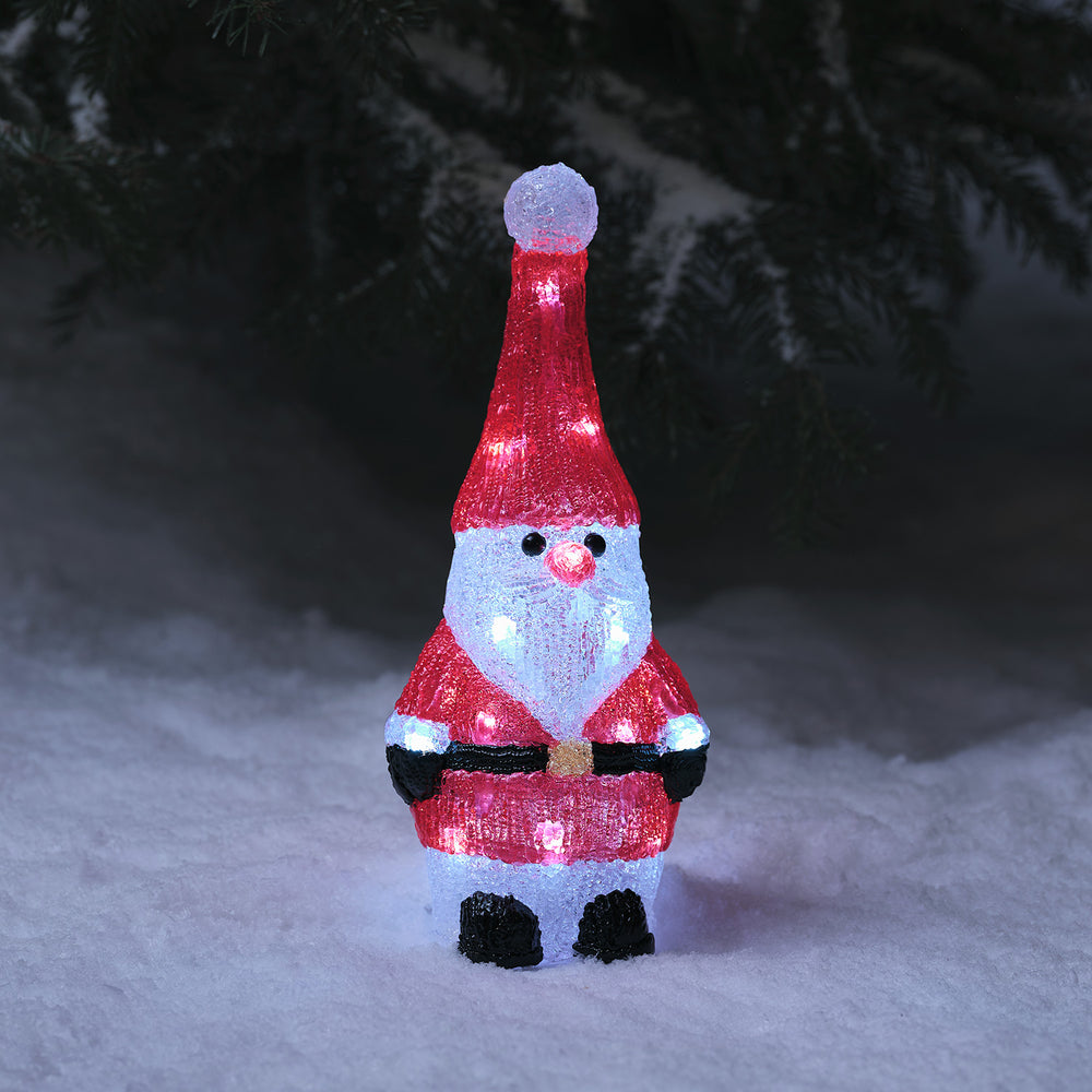 Leuchtender Acryl Weihnachtsmann mit roter Mütze und Anzug steht im Schnee bei Dunkelheit
