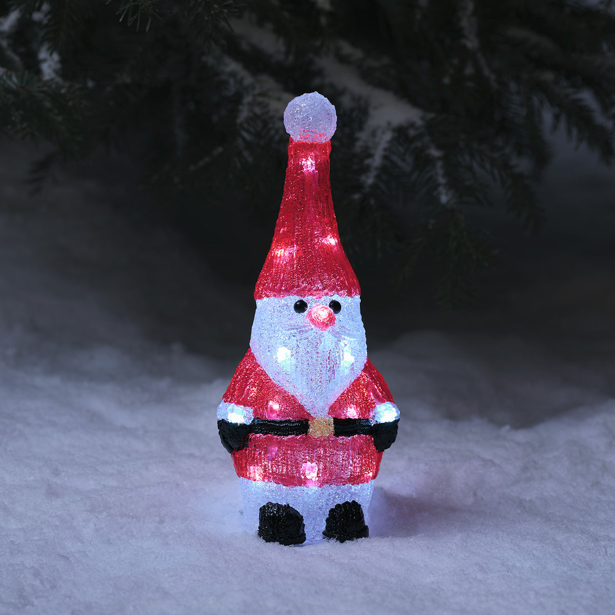Leuchtender Acryl Weihnachtsmann mit roter Mütze und Anzug steht im Schnee bei Dunkelheit