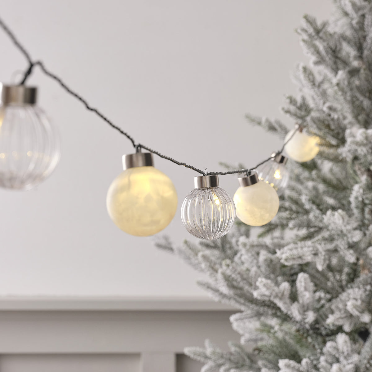 Nahaufnahme LED Lichterkette mit warmweißen und klaren Weihnachtsbaumkugeln an grünem Kabel