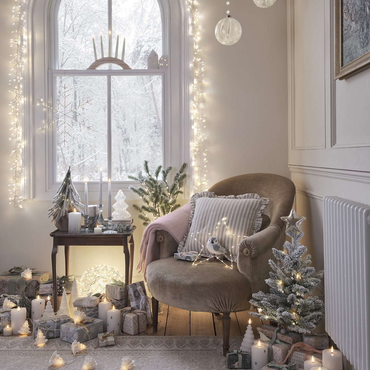 Wohnzimmer mit Lichterketten am Fensterrahmen, Sessel und weihnachtlicher Dekoration