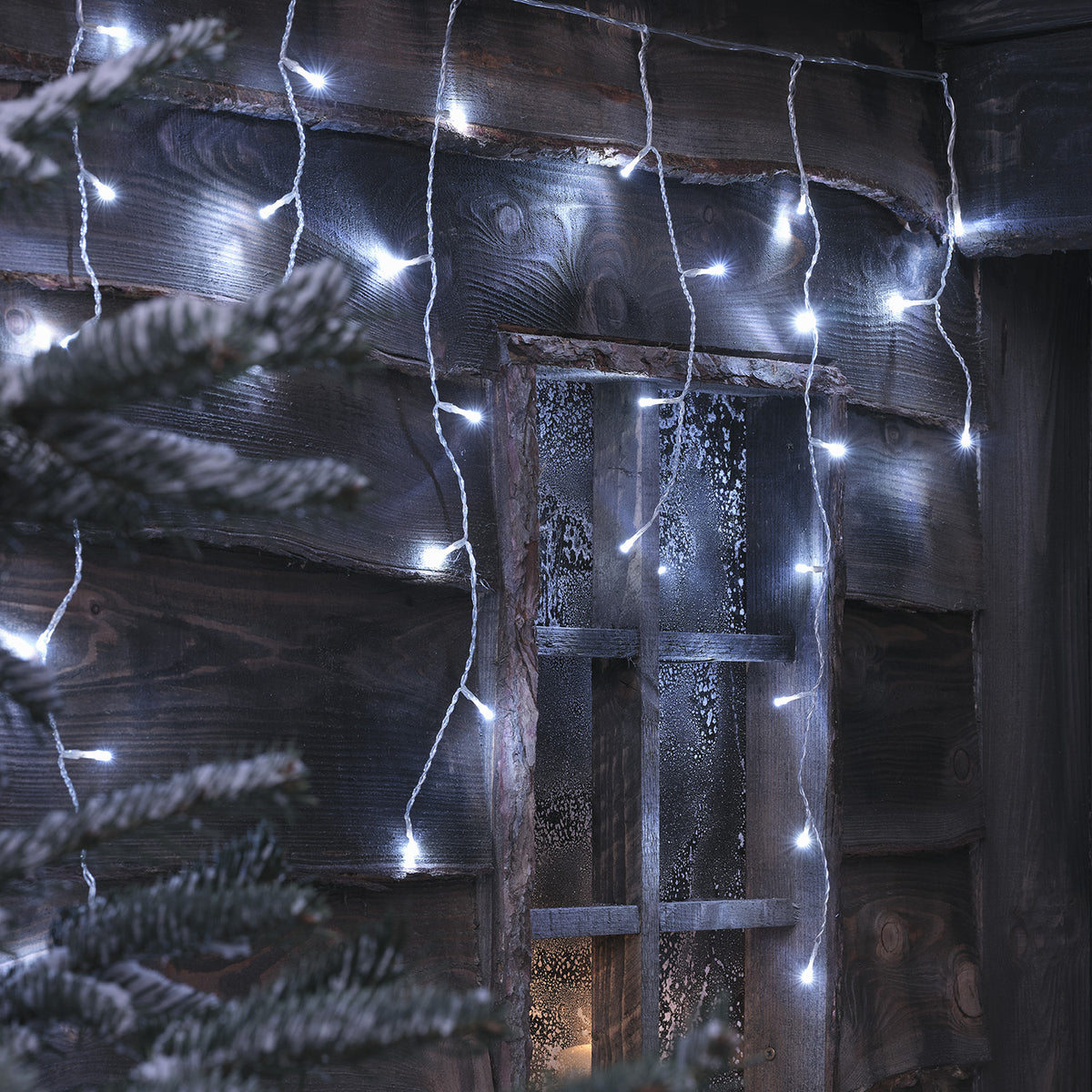 Bicolor LED Eiszapfen Lichterkette in kaltweiß an Holzfassade mit Fenster und Tannenzweig