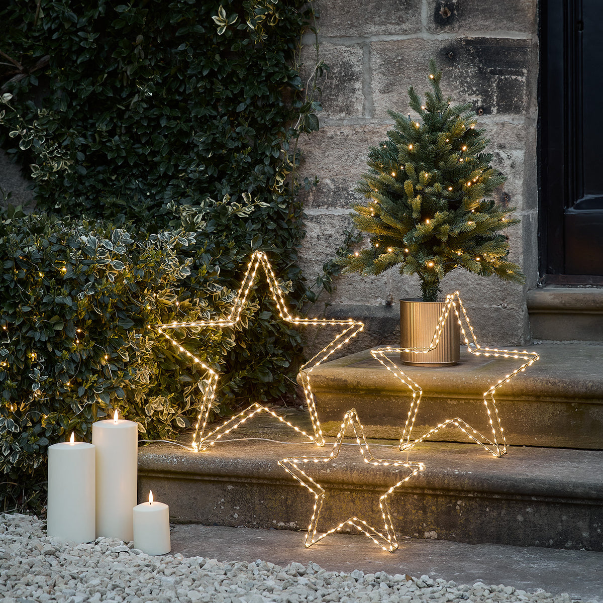 Drei Micro LED Sterne neben einem kleinen Weihnachtsbaum auf einer Steintreppe mit brennenden Kerzen