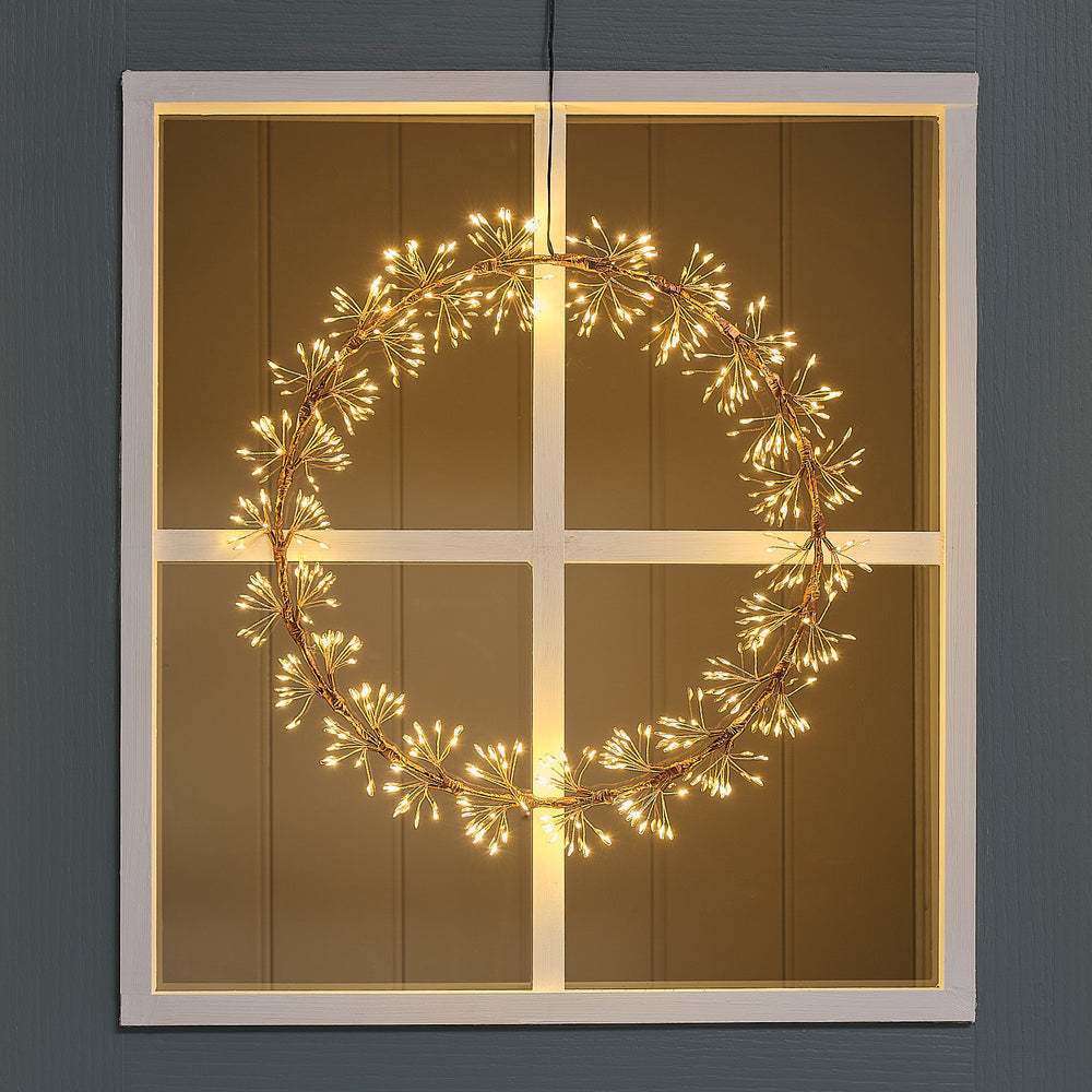 Beleuchteter LED-Starburst-Kranz außen an Fenster mit goldfarbenem Ring und warmweißen LEDs