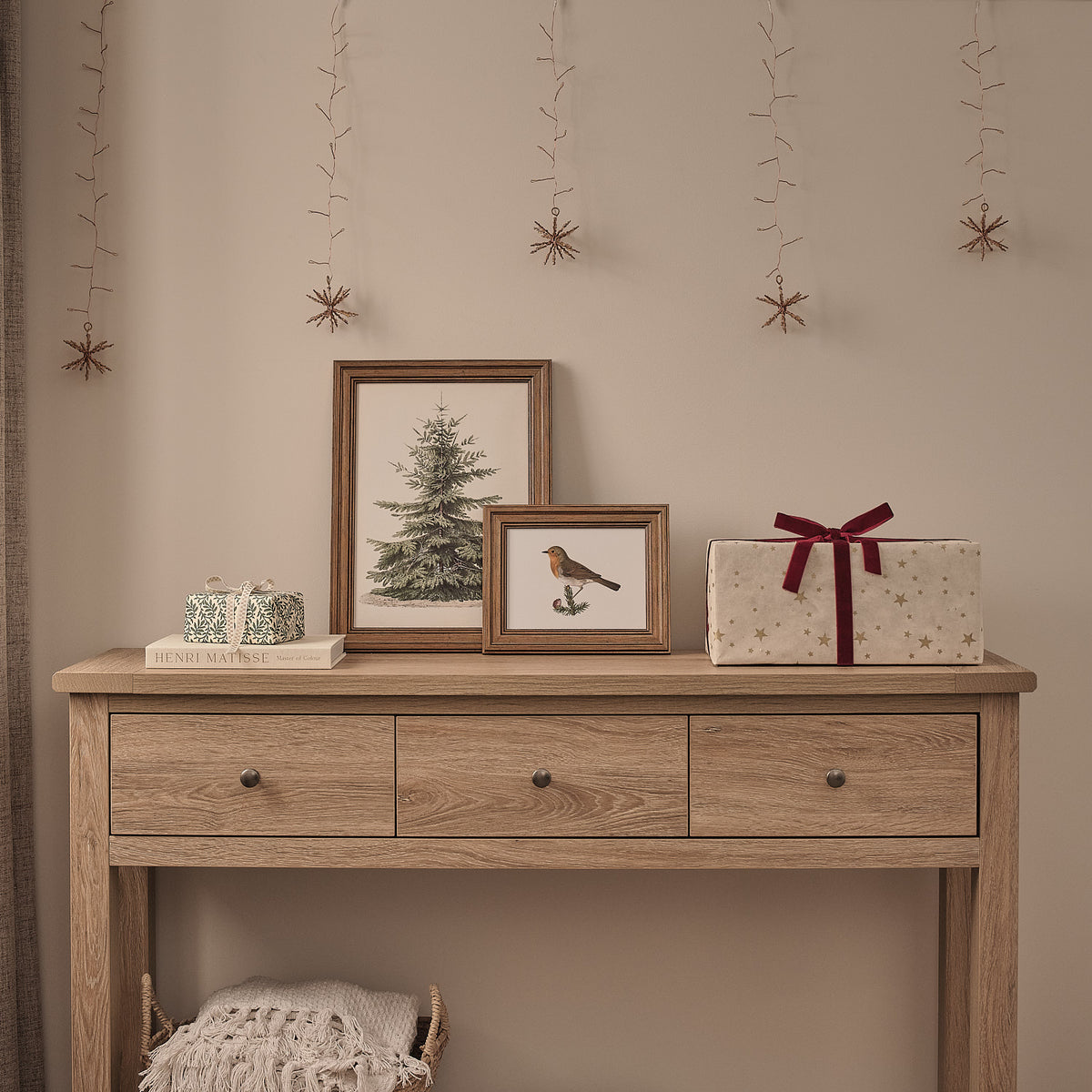 Goldener LED Lichtervorhang mit unbeleuchteten Starburst-Clustern über Holzkommode mit Weihnachtsbildern