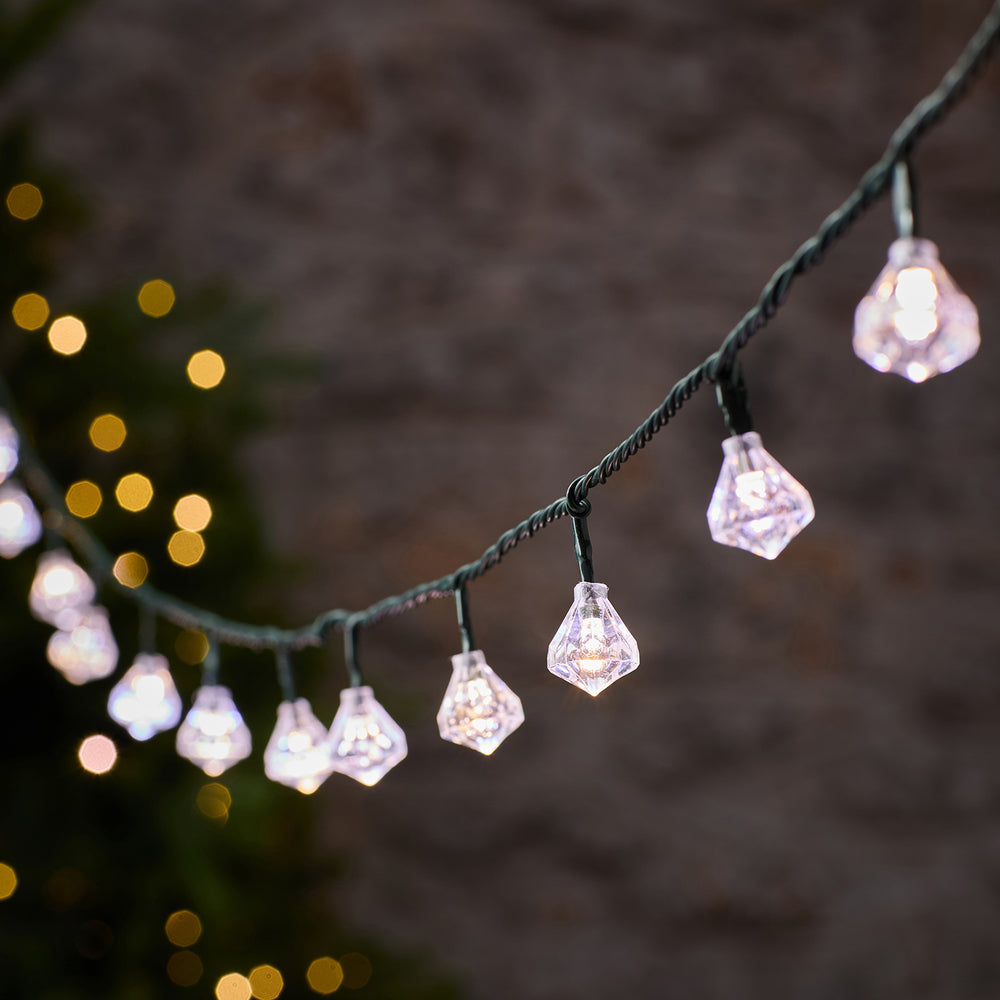 LED-Lichterkette mit weißen Diamantkappen an grünem Kabel vor unscharfem Hintergrund