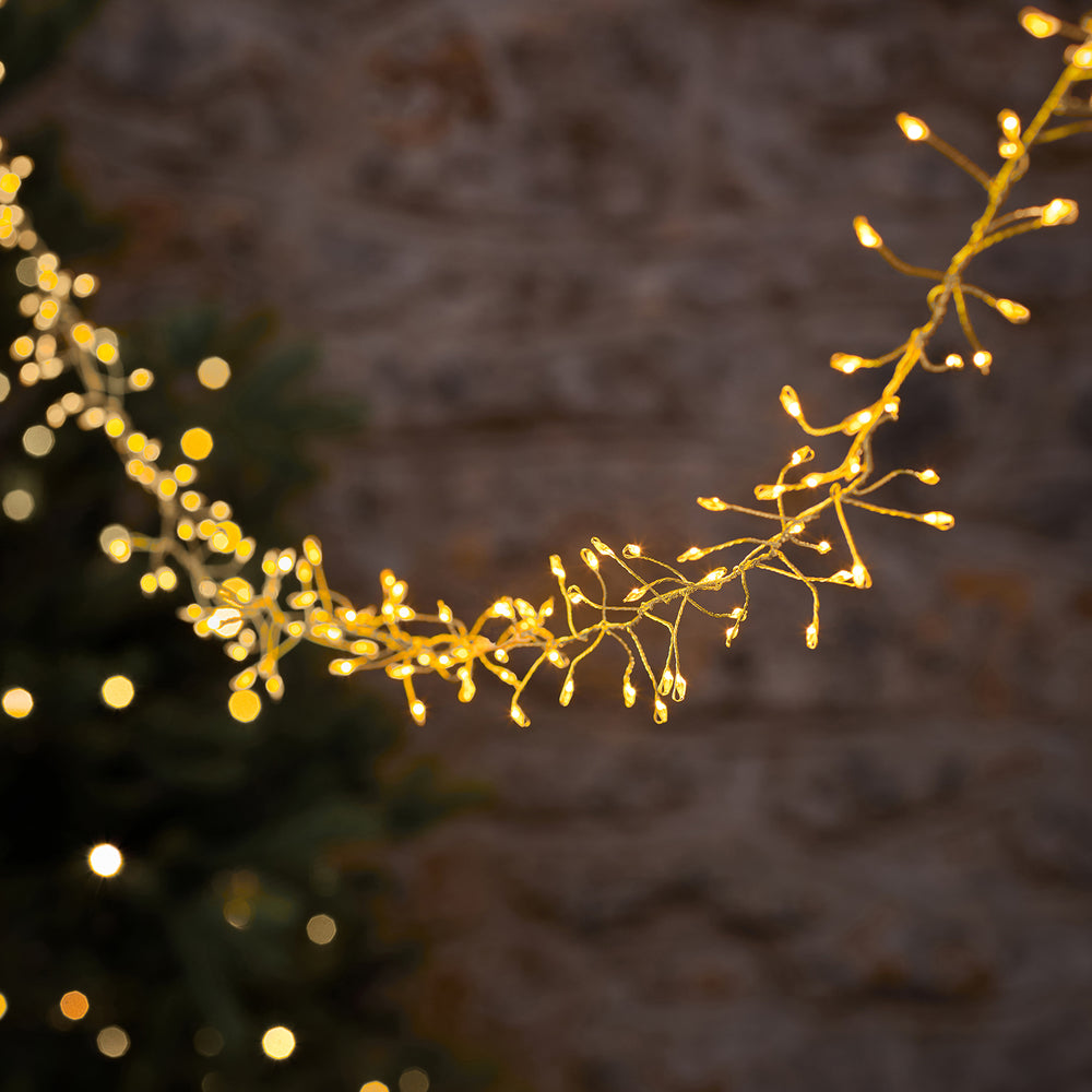 Goldene LED-Cluster-Lichterkette mit warmweißen Mikro-LEDs leuchtet vor unscharfem Hintergrund