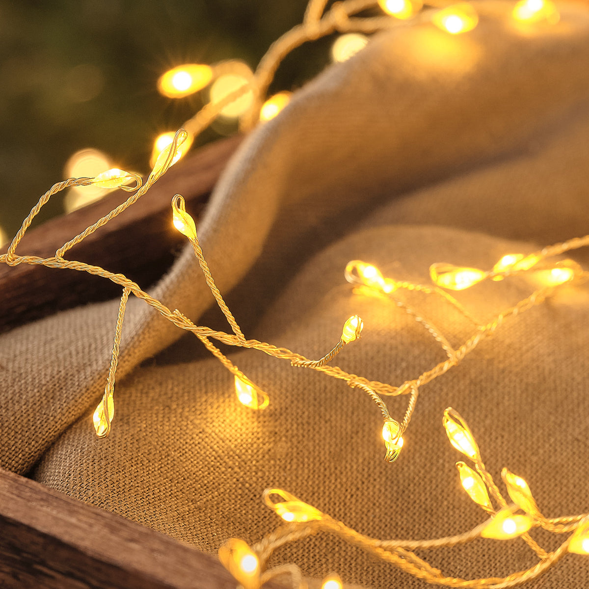 Leuchtende Mikro-LEDs der goldenen Lichterkette auf grauem Stoff in Holzkiste